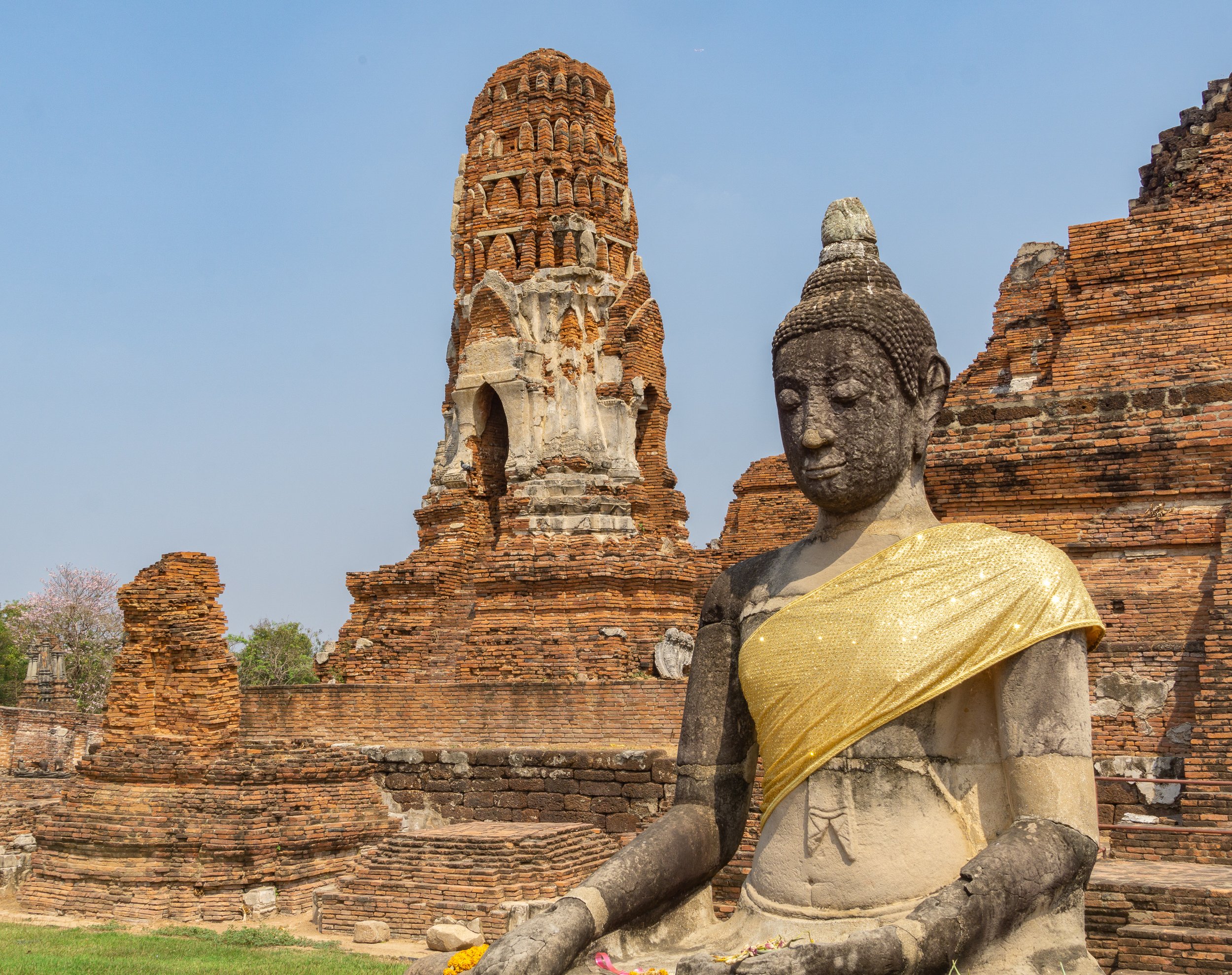 Ancient Buddha statue draped in a golden ceremonial robe among the historic temple ruins of Ayutthaya, Thailand.