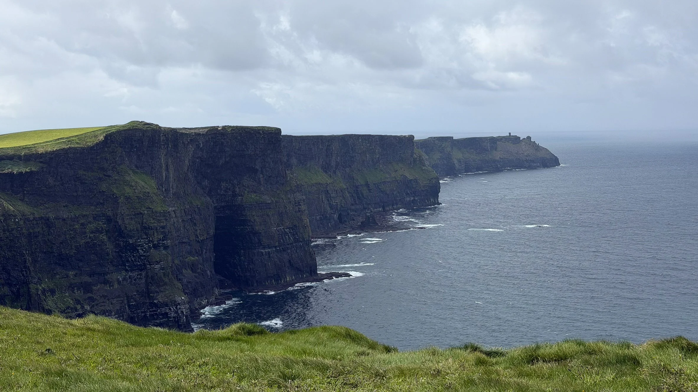 The Cliffs of Moher rise dramatically above the Atlantic Ocean beneath brooding clouds, revealing the rugged beauty of Ireland's west coast in County Clare.