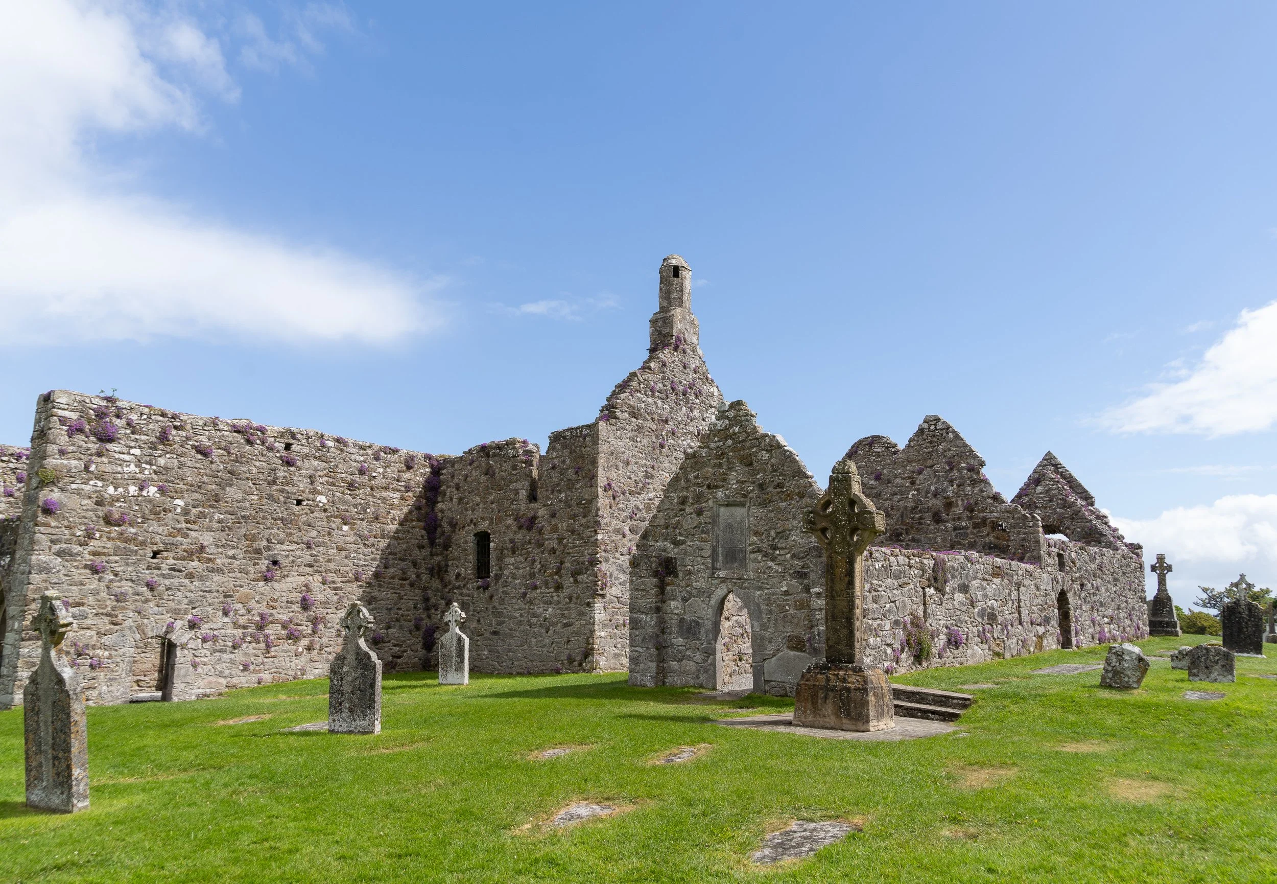 Ancient stone Clonmacnoise Monastery ruins with Celtic crosses and a historic graveyard beneath a bright blue sky in Ireland.