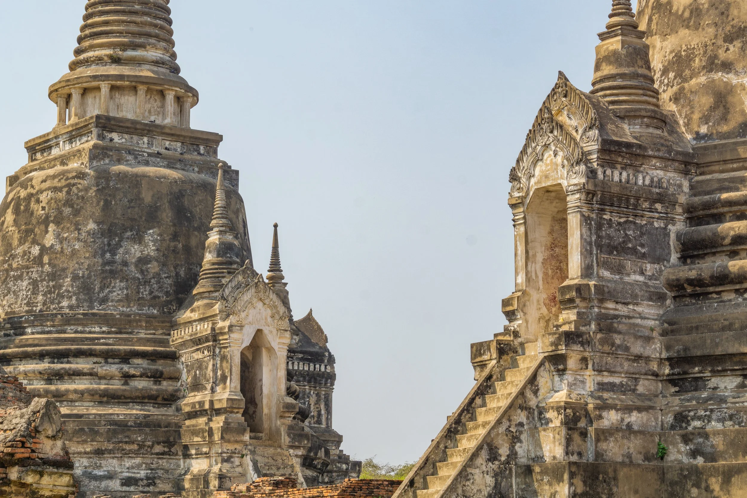 Historic brick stupas and temple ruins at Ayutthaya Historical Park under a hazy sky.