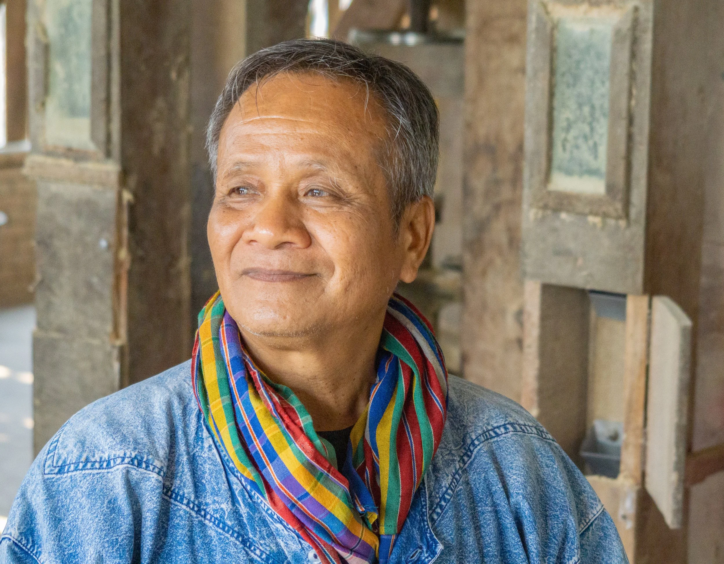 Portrait of an older man wearing a colorful scarf inside a traditional village in northern Thailand.