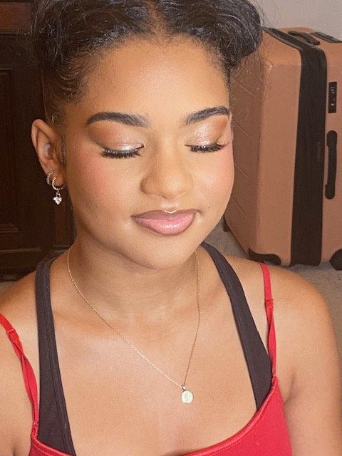 A young woman with makeup, wearing a black top with red straps, and jewelry including earrings and a necklace, with closed eyes and a neutral expression.