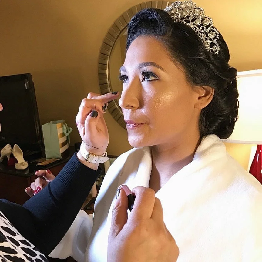 A woman getting ready, with a tiara on her head and makeup being applied, likely on her wedding day.