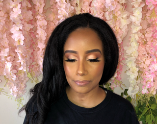 A woman with long black hair and makeup, standing in front of pink floral backdrop.