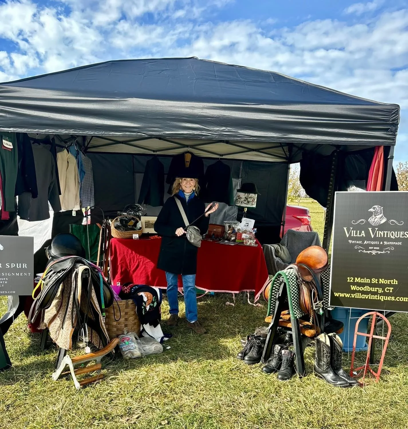 Marlyn Henry at Bethlehem Land Trust’s annual Hunter Pace stall with clothing, shoes, and accessories displayed on tables and hanging from the tent. The sign reads 'Villa Vintiques' and provides the address in Woodbury, CT.