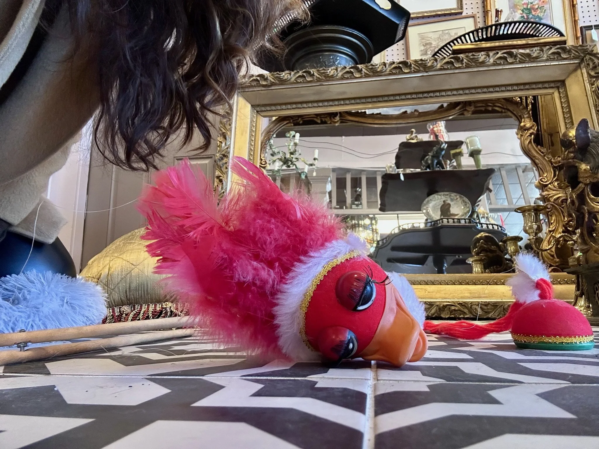 A vintage 1960s red bird puppet with feathers and pompoms lying on our black and white tiled floor in Villa Vintiques.