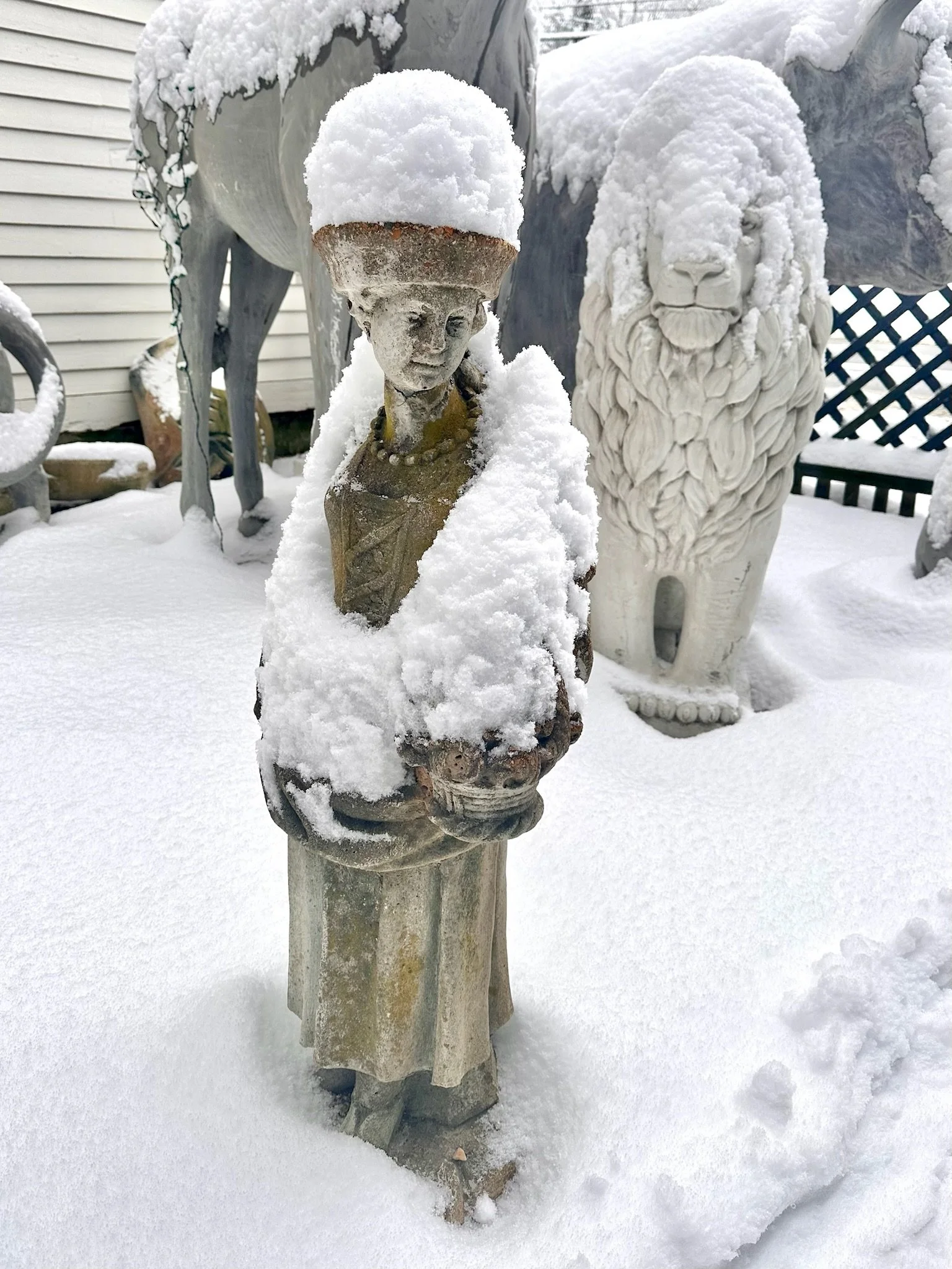 Winter in the courtyard between the 2 historic buildings that make up Villa Vintiques. Snow-covered outdoor sculptures and statues including a small carved figure with a hat, a lion with a flowing mane