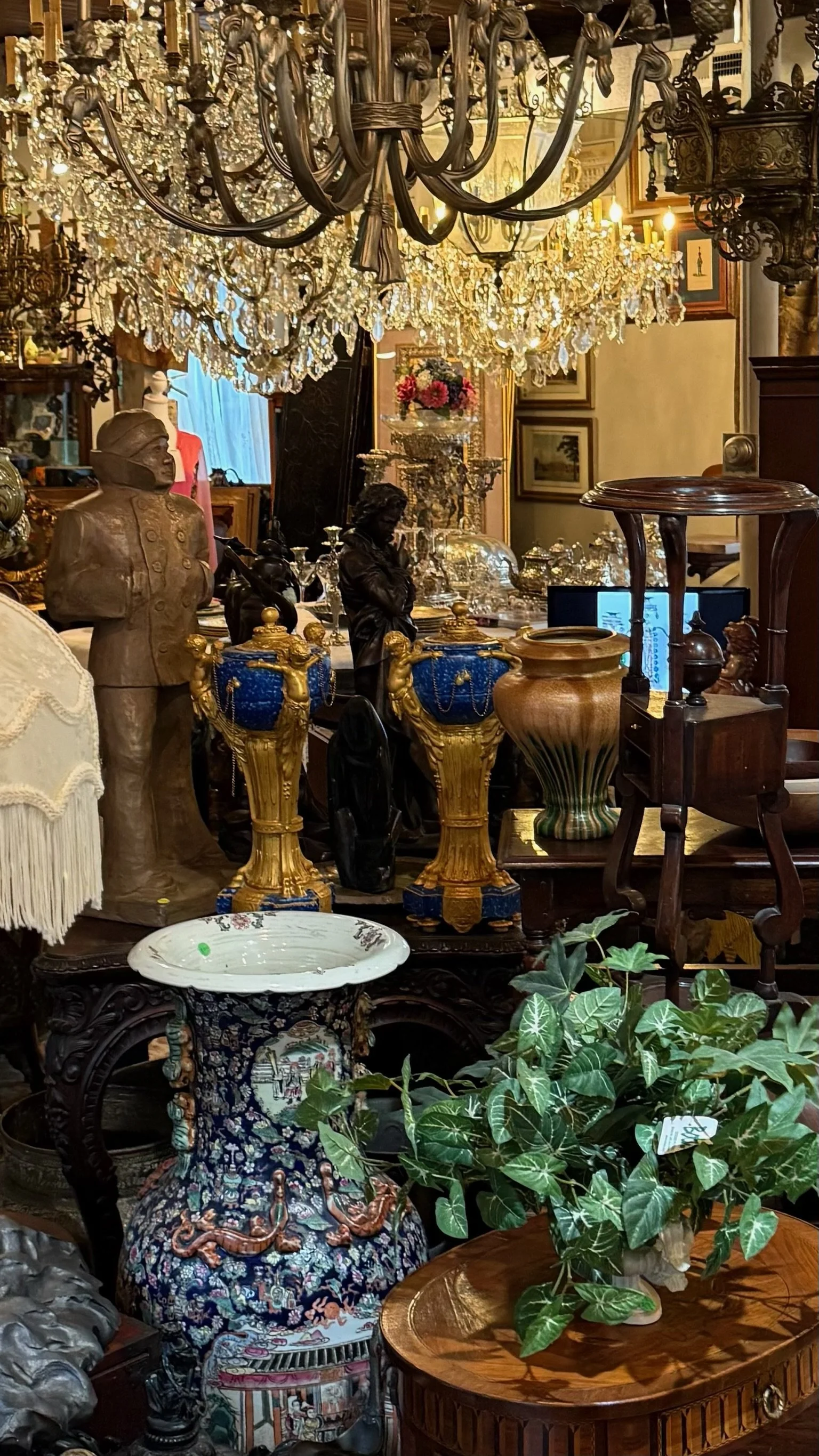 Interior of Villa Vintiques, showing our crystal chandeliers, sculptures, vases, and various vintage furniture and decor items, including a bust statue, ornate tables, and framed paintings.