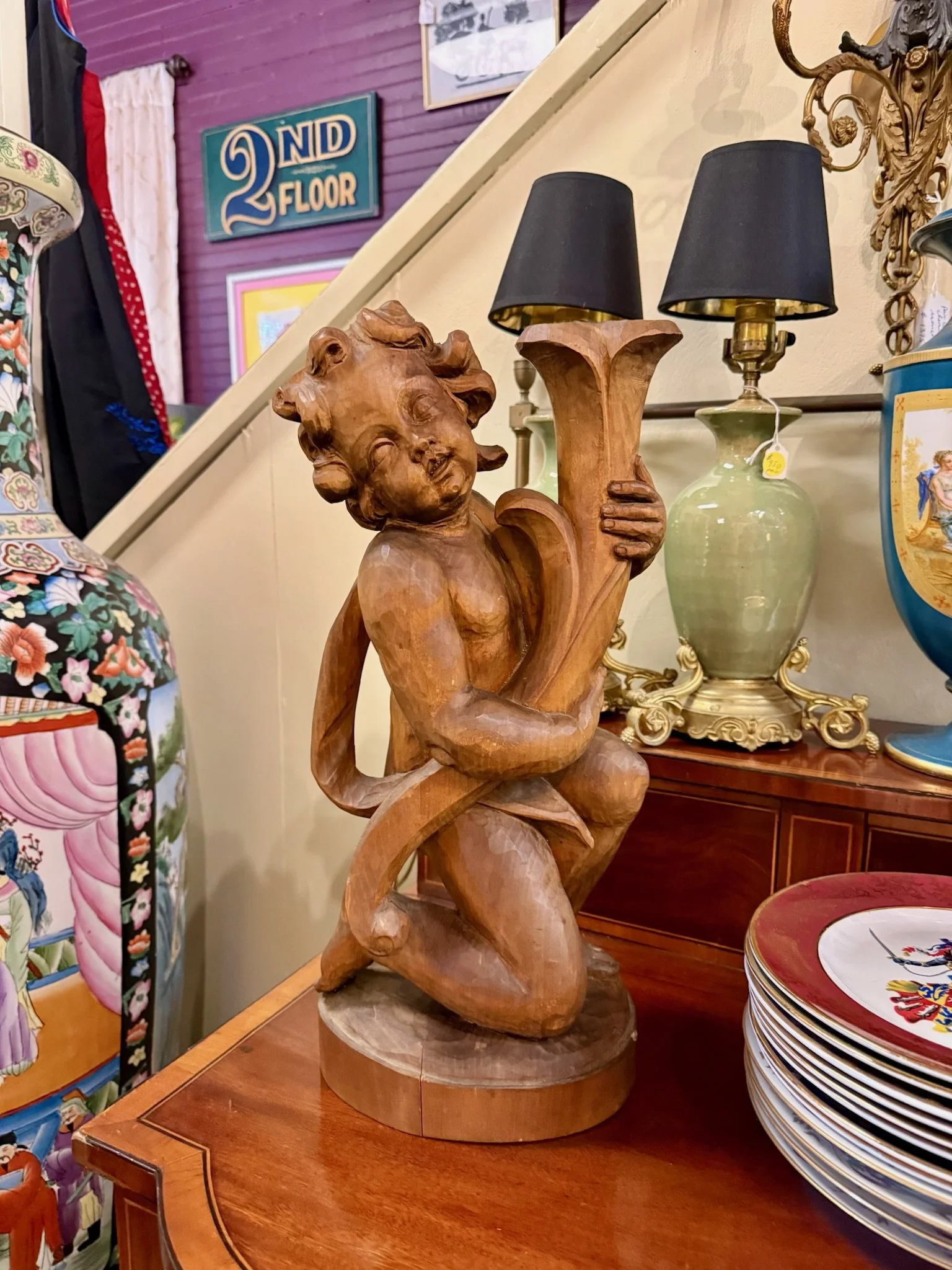 Wooden sculpture of a cherub or puti for sale at VIlla Vintiques, placed on a wooden table surrounded by decorative lamps and china dishware.