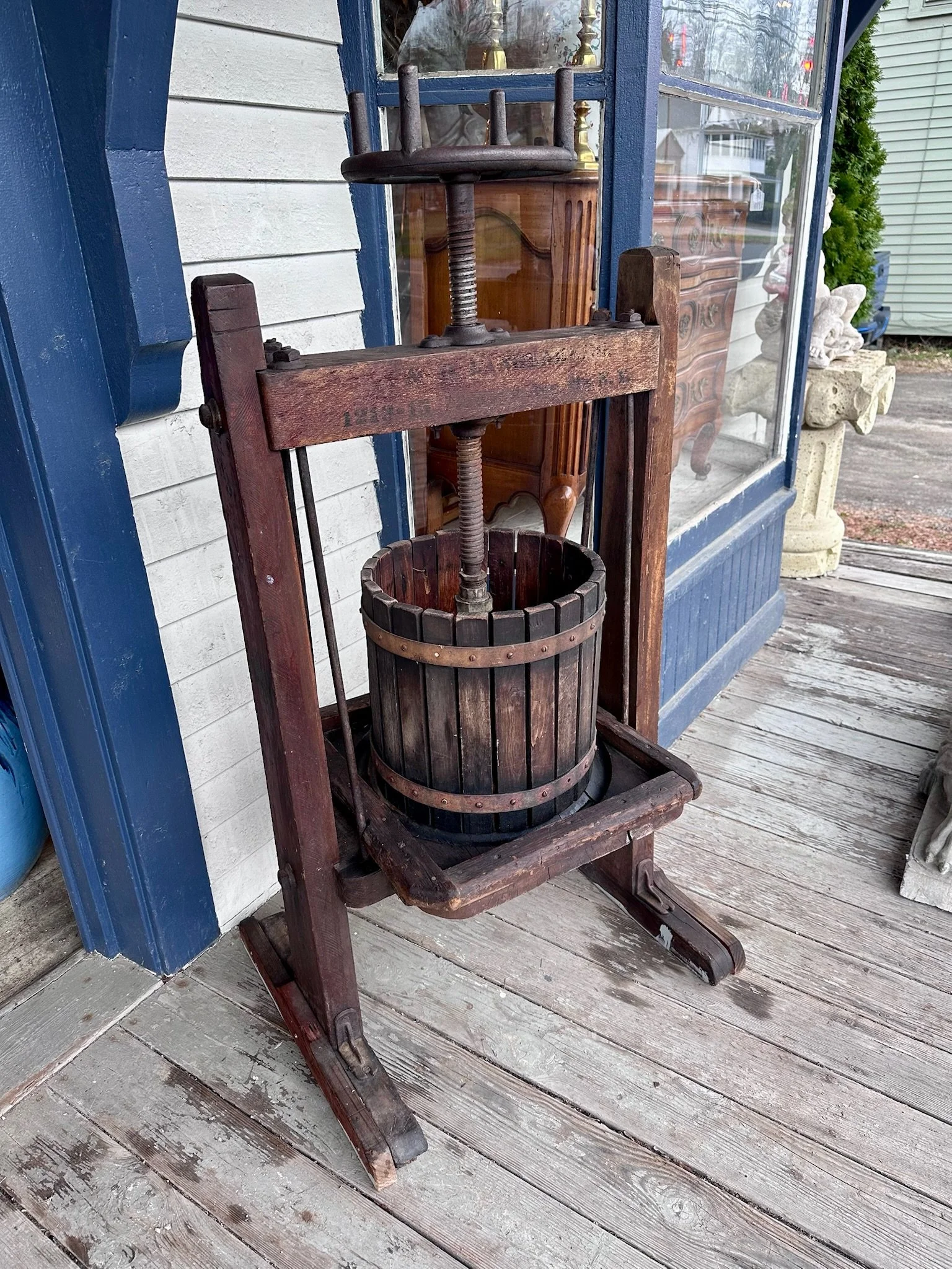 An old wooden grape press with a large screw mechanism inside a wooden barrel, positioned on a rustic wooden platform at Villa Vintiques.
