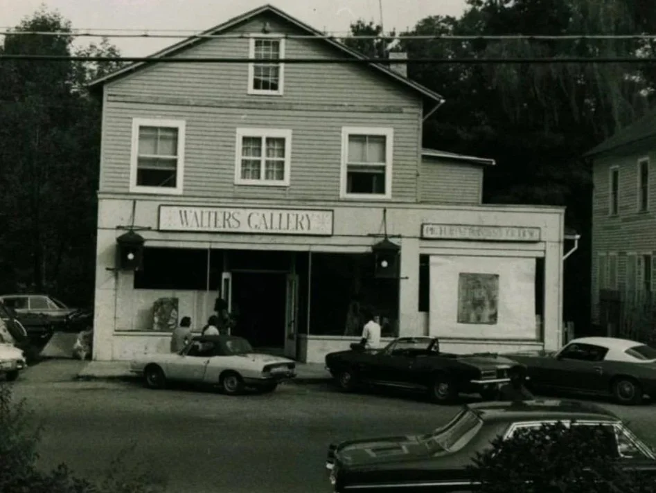 A vintage black and white photo of Walters Gallery, a two-story building with cars parked in front and people standing near the entrance.