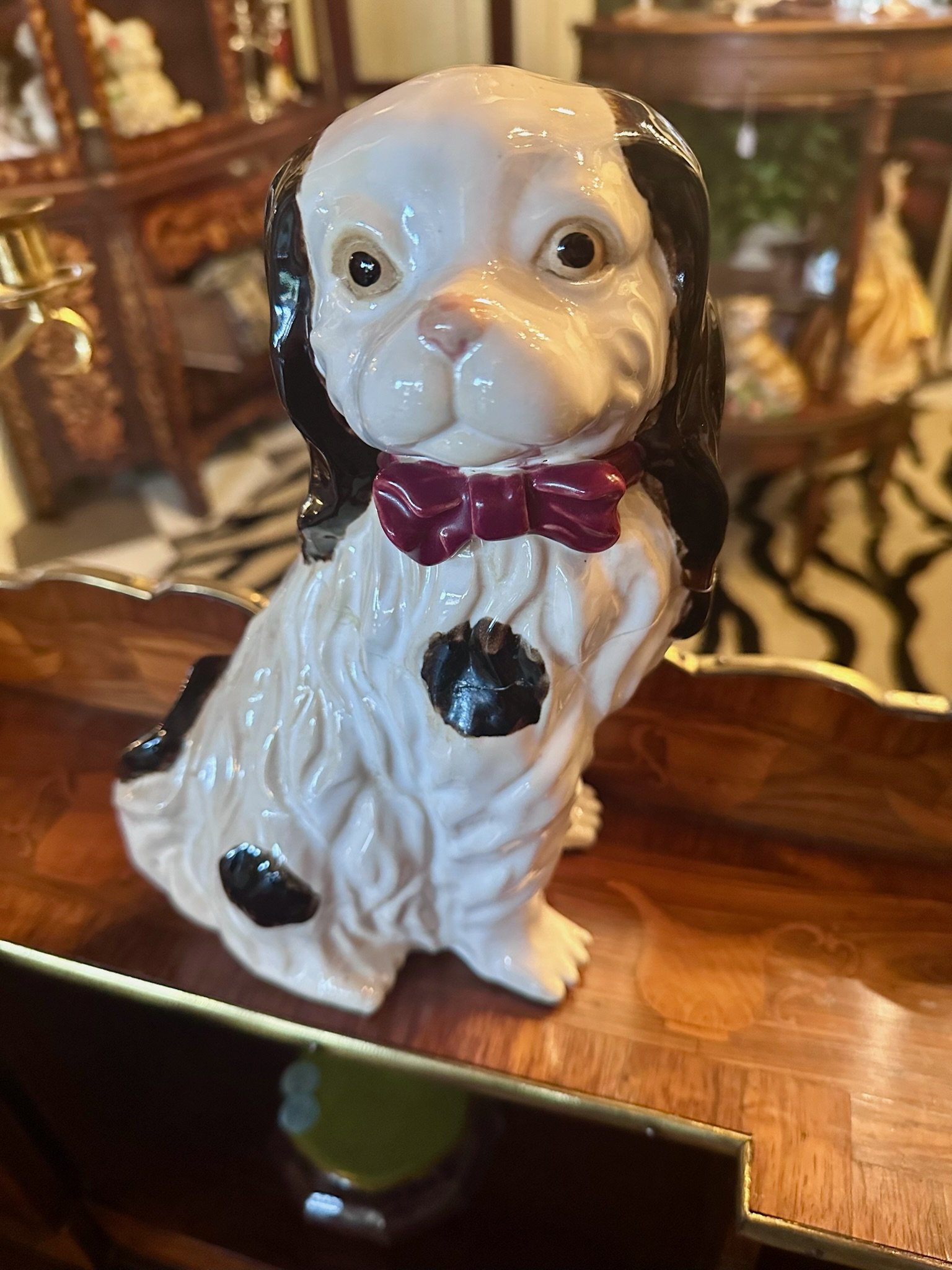 Single Staffordshire porcelain dog figurine wearing a red bow tie, positioned on a wooden surface for sale inside Villa Vintiques.