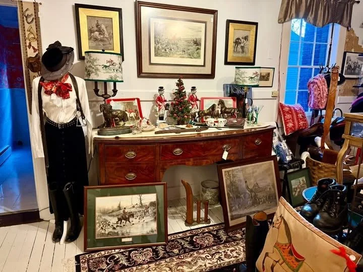 A vintage-style room with framed black-and-white and colored artwork on the walls, a red wooden sideboard decorated for Christmas with small Santa figurines and a miniature Christmas tree, and various antique and decorative items including paintings,