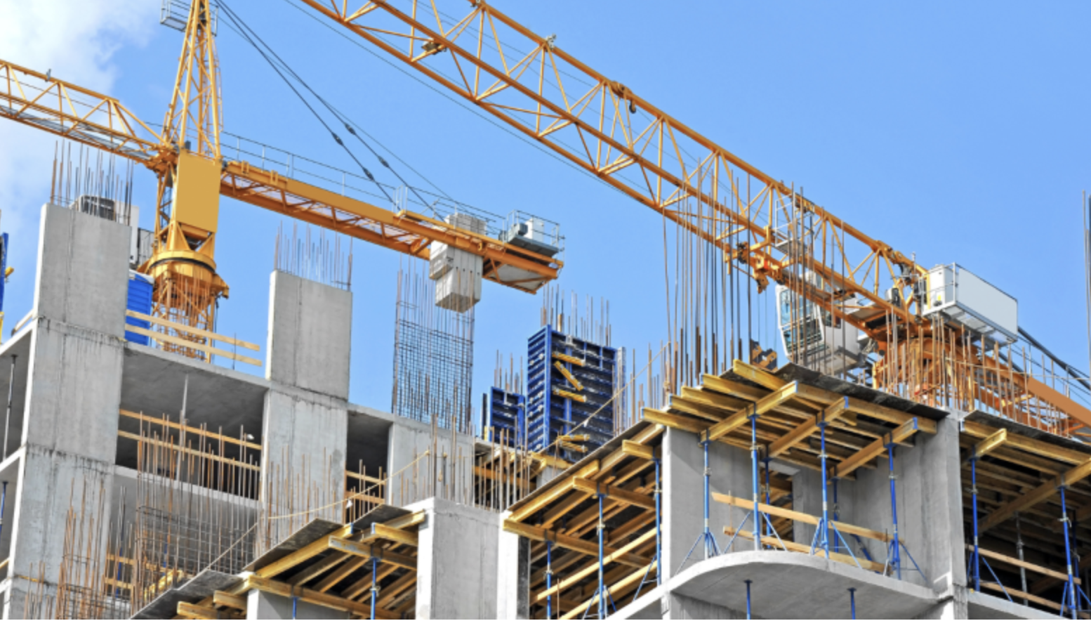 Construction site with a large yellow crane and concrete building framework under blue sky.
