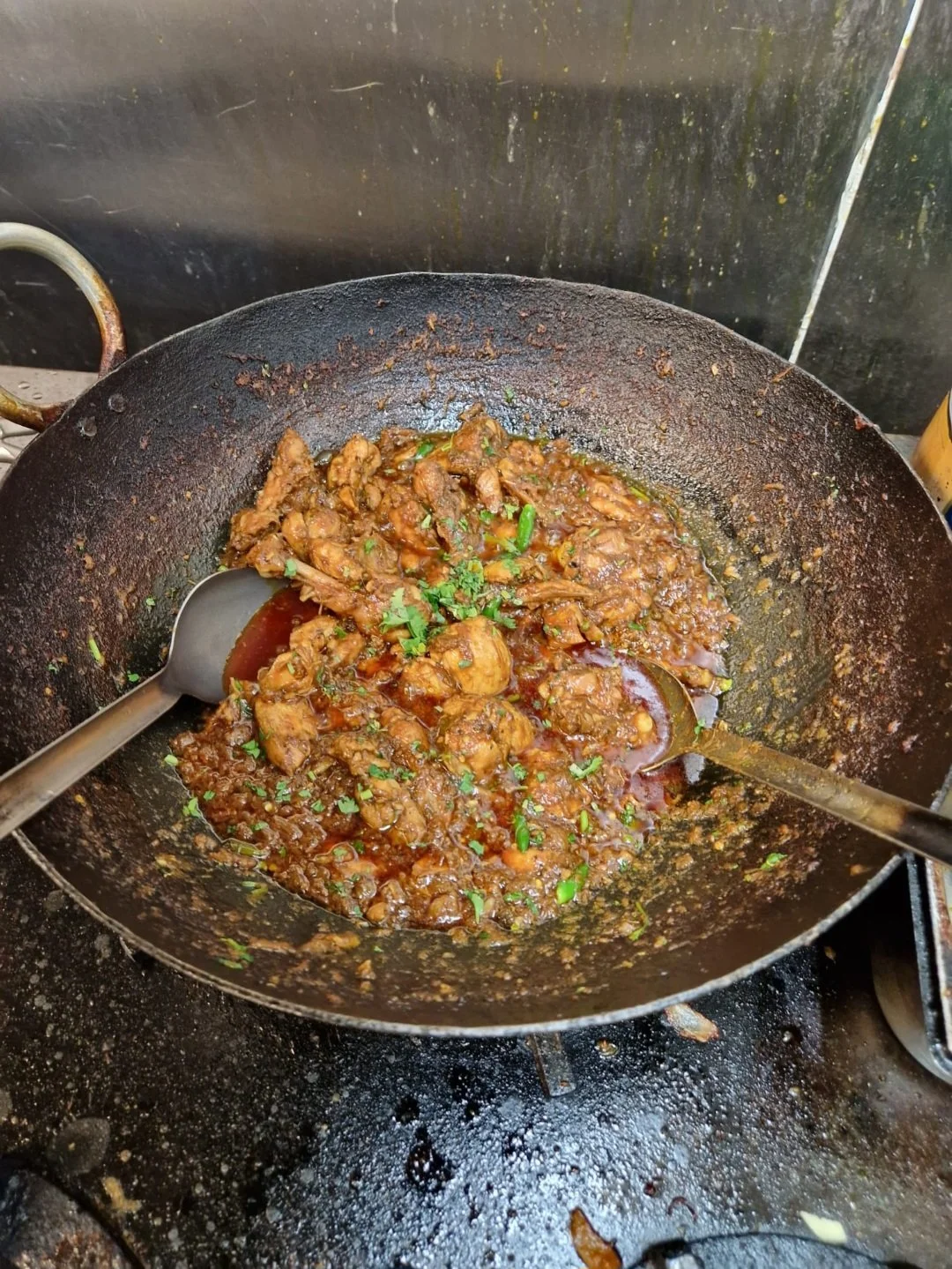 Stir-fried chicken in a dark sauce with chopped green herbs in a black wok.
