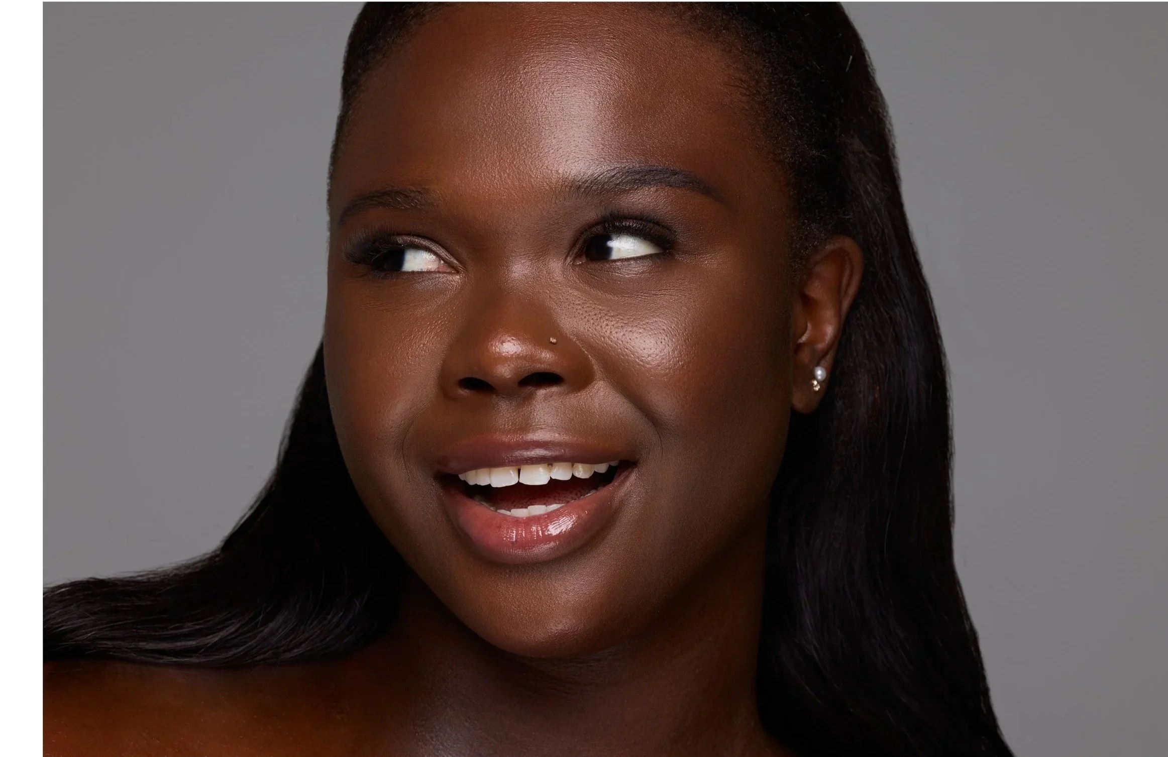 Close-up of a smiling Black woman with dark hair, wearing pearl earrings, against a gray background.