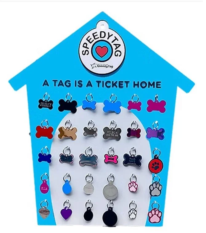 Display of various pet tags in different shapes and colors hanging inside a house-shaped display with the message "A TAG IS A TICKET HOME" at the top.