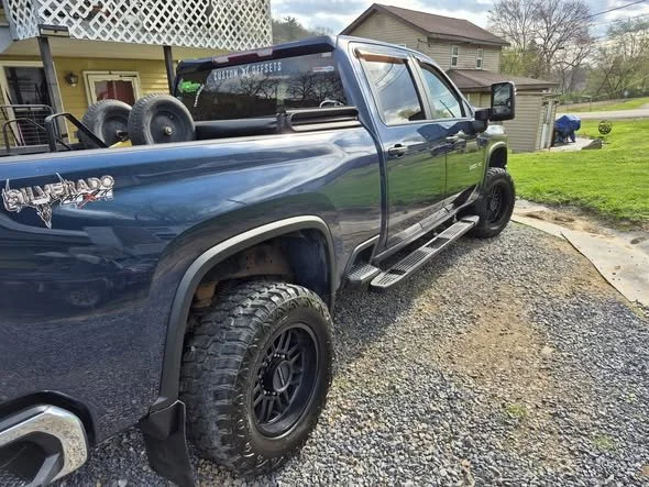 Blue Toyota Tundra pickup truck parked on gravel driveway in front of a house with a porch and a lawn.