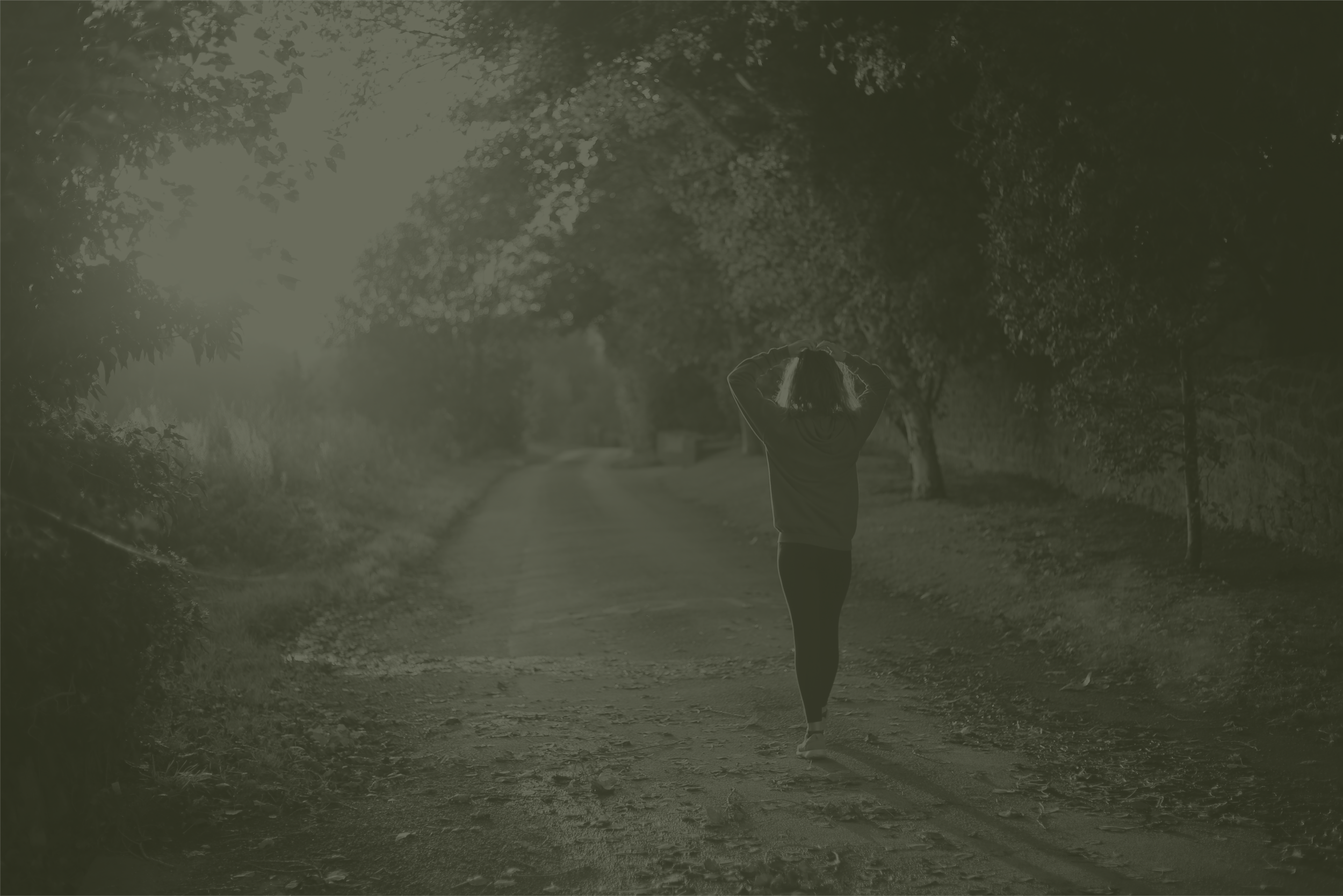 A person jogging or walking on a path surrounded by trees with sunlight filtering through the leaves in the background.