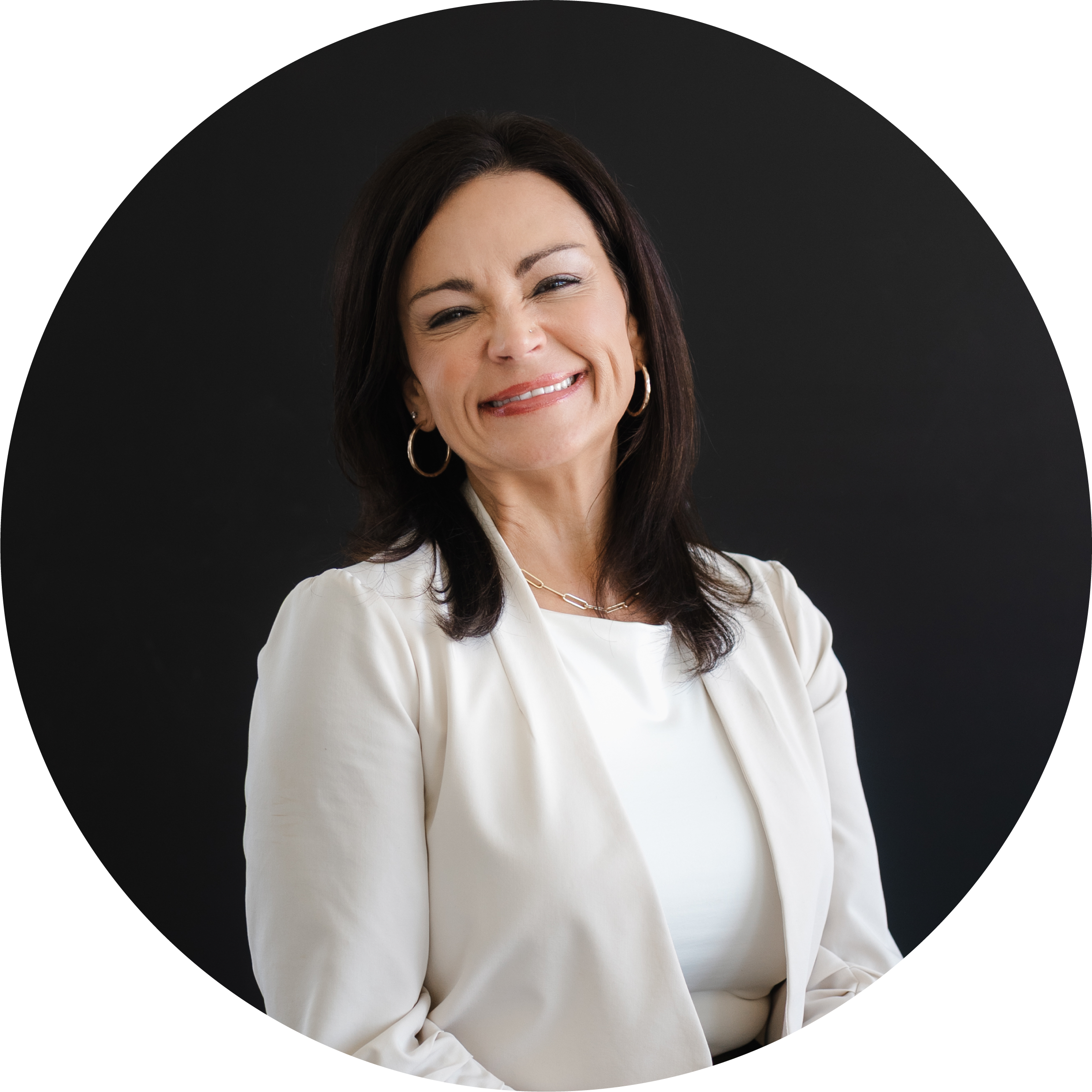 Jamie Stice, FNP-C | Smiling woman with dark hair, wearing a white blazer and hoop earrings, standing against a dark background.
