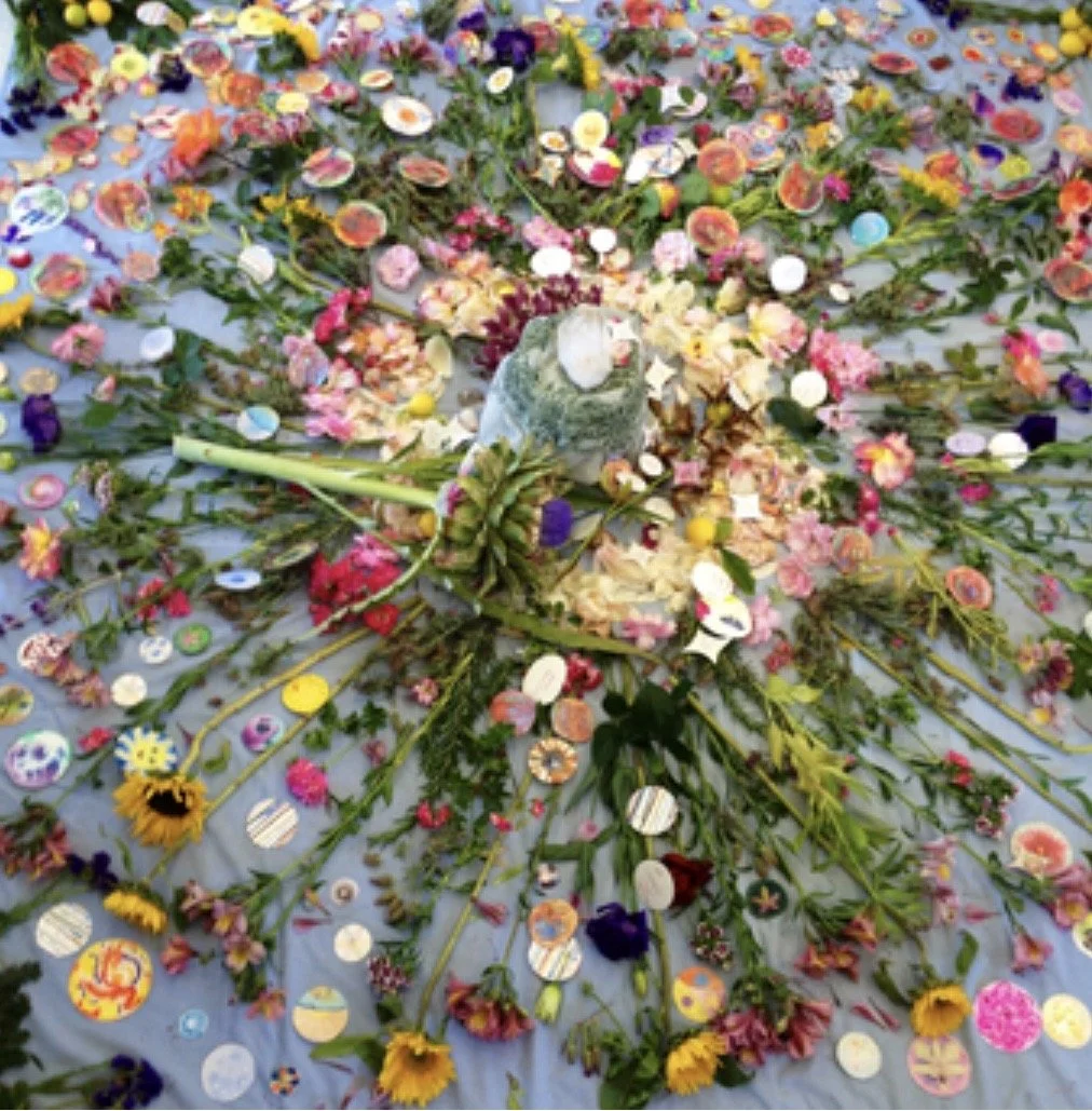 Colorful floral and candy arrangement with a bird in the center, surrounded by flowers, petals, and various candies on a light blue surface.