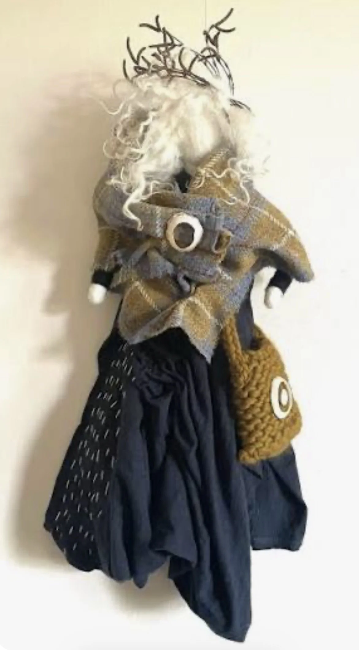 A mixture of clothing and accessories hanging on a wall, including a plaid shirt, a dark jacket, a backpack, a scarf, and a hat with antlers attached.