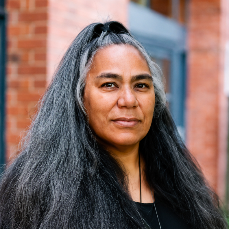 Portrait of a woman with long, gray and black hair outside a brick building
