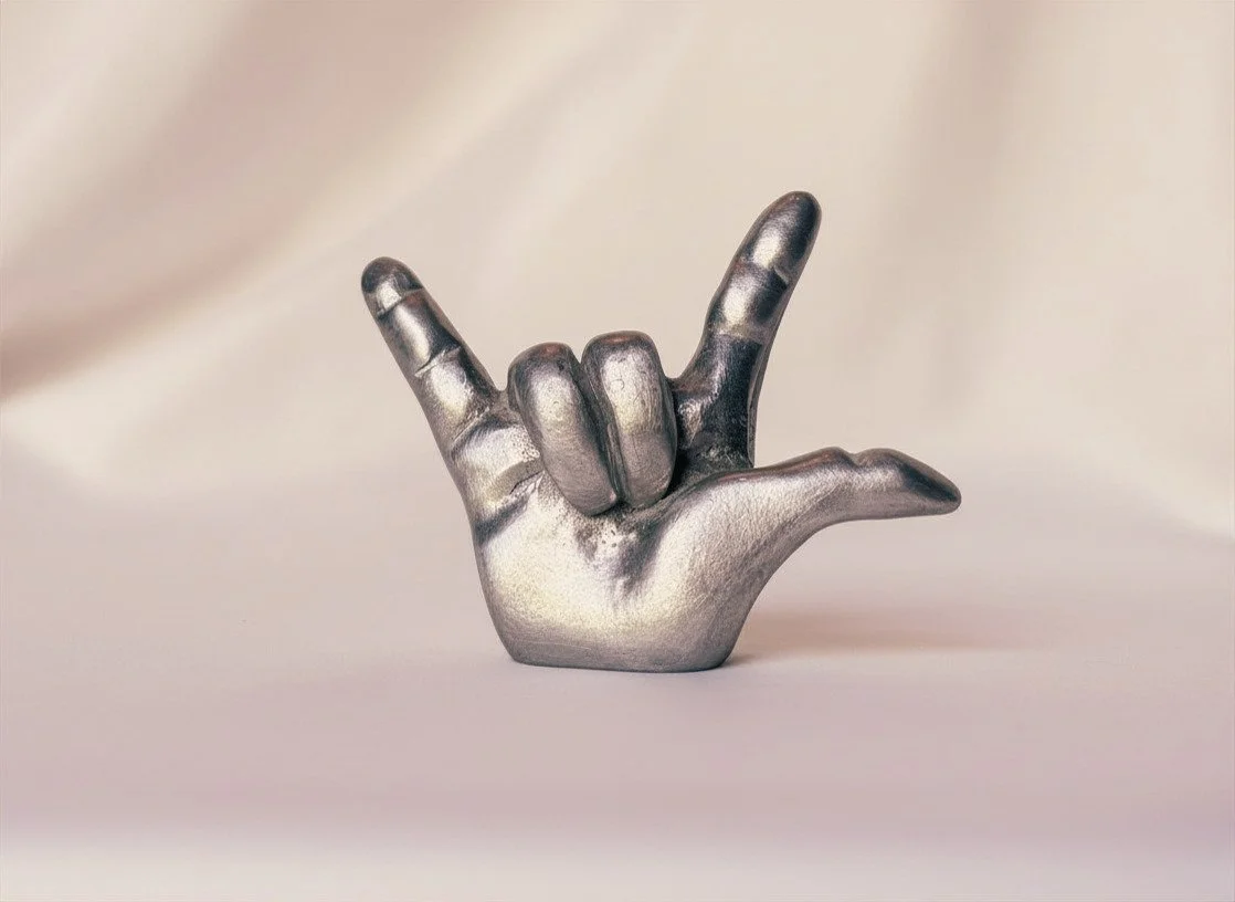 Silver metallic sculpture of a hand making the I love you gesture isolated on a white background.