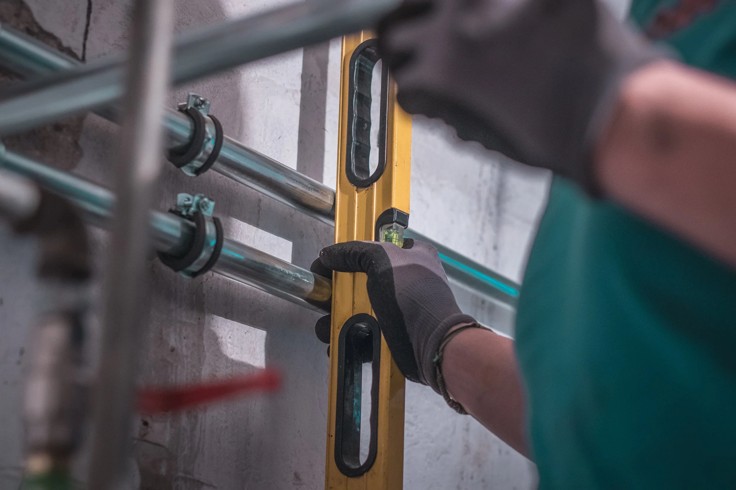 Person measuring properly aligned pipes using a yellow level tool.