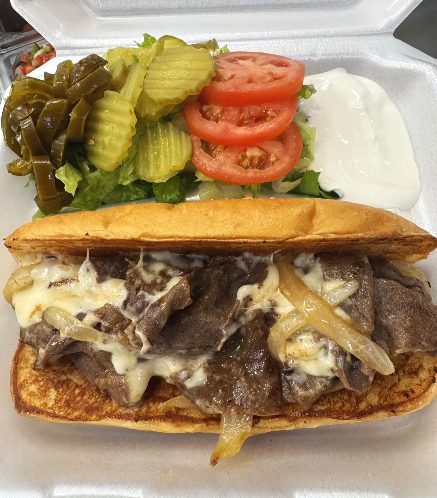 A cheesesteak sandwich with cooked beef, melted cheese, and onions in a toasted sub roll.