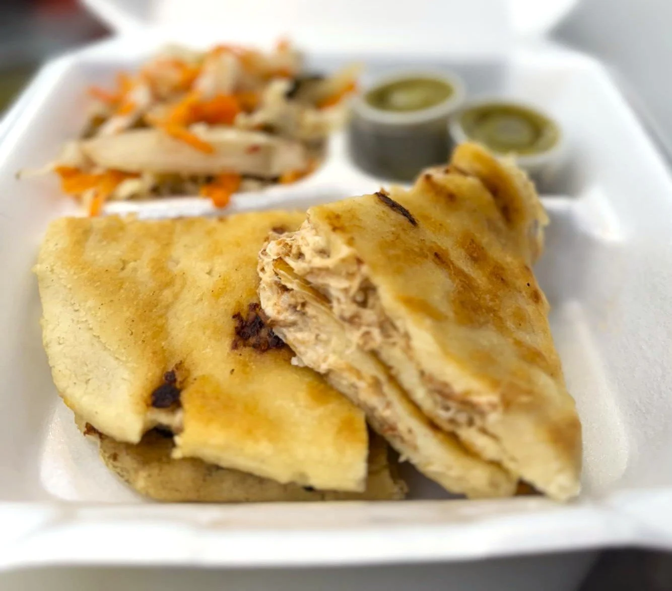 Papusa with melting cheese, side of shredded cabbage and carrots, and two small containers of green salsa