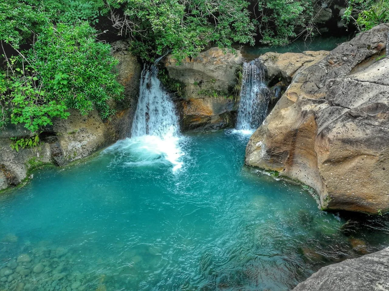Small waterfalls cascading into a turquoise pool surrounded by rocks and lush green foliage.