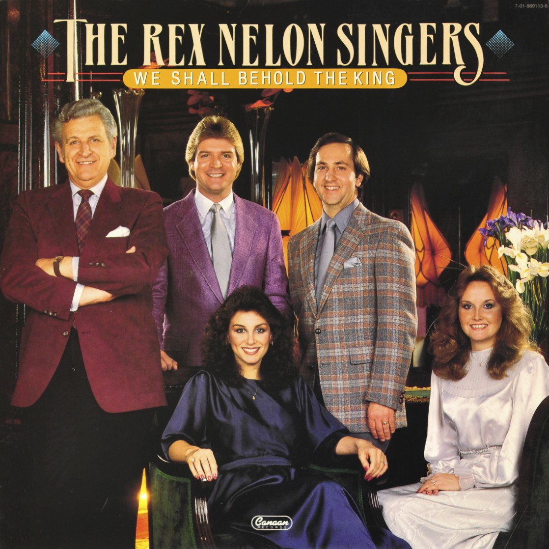 Album cover for The Rex Nelson Singers titled 'We Shall Behold the King' featuring six people dressed in formal clothes, with three standing in the background and two sitting in front, in a room with warm lighting and floral arrangements.