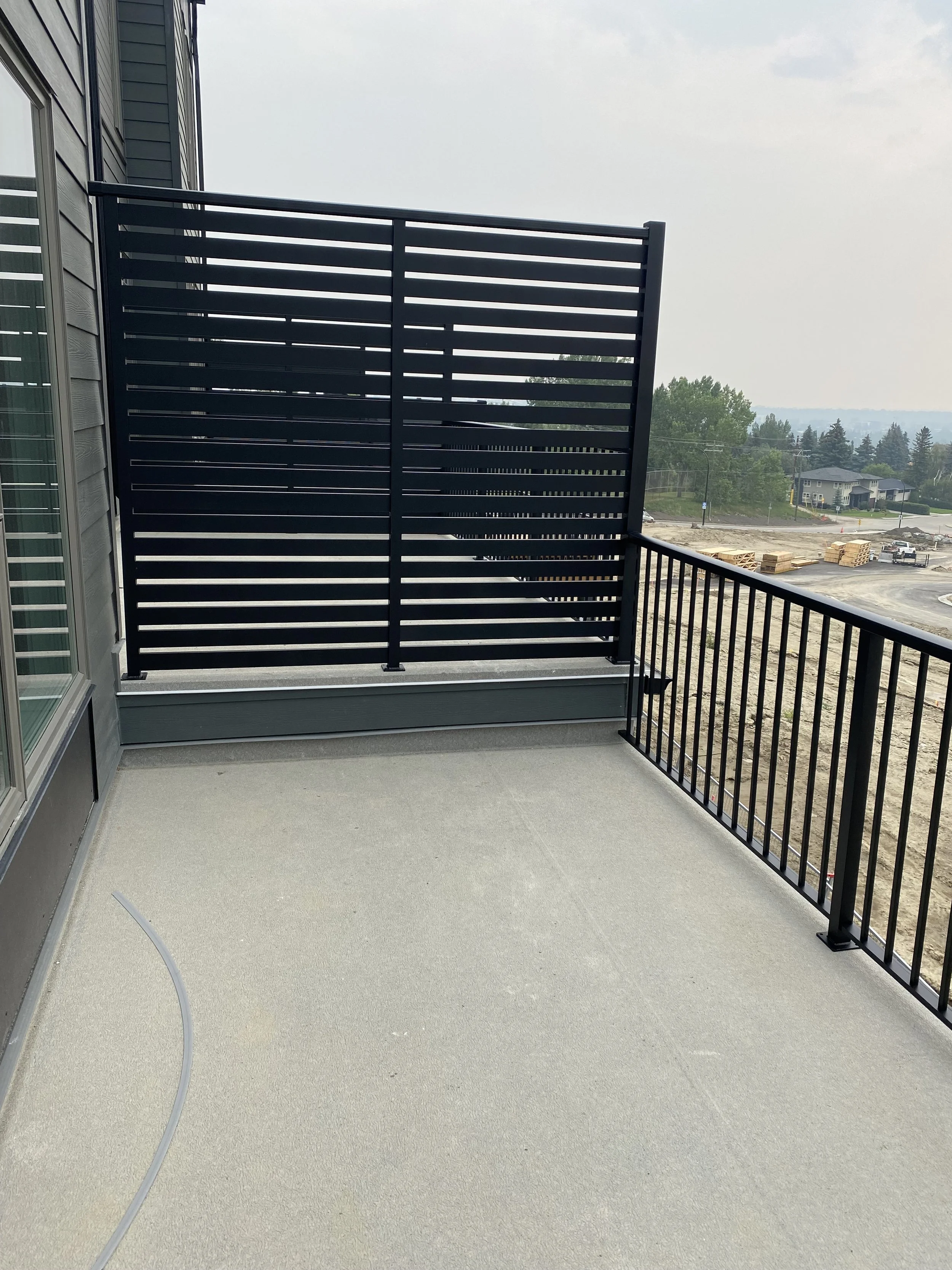 Balcony with a black metal railing and a privacy screen, overlooking a construction site and neighborhood.
