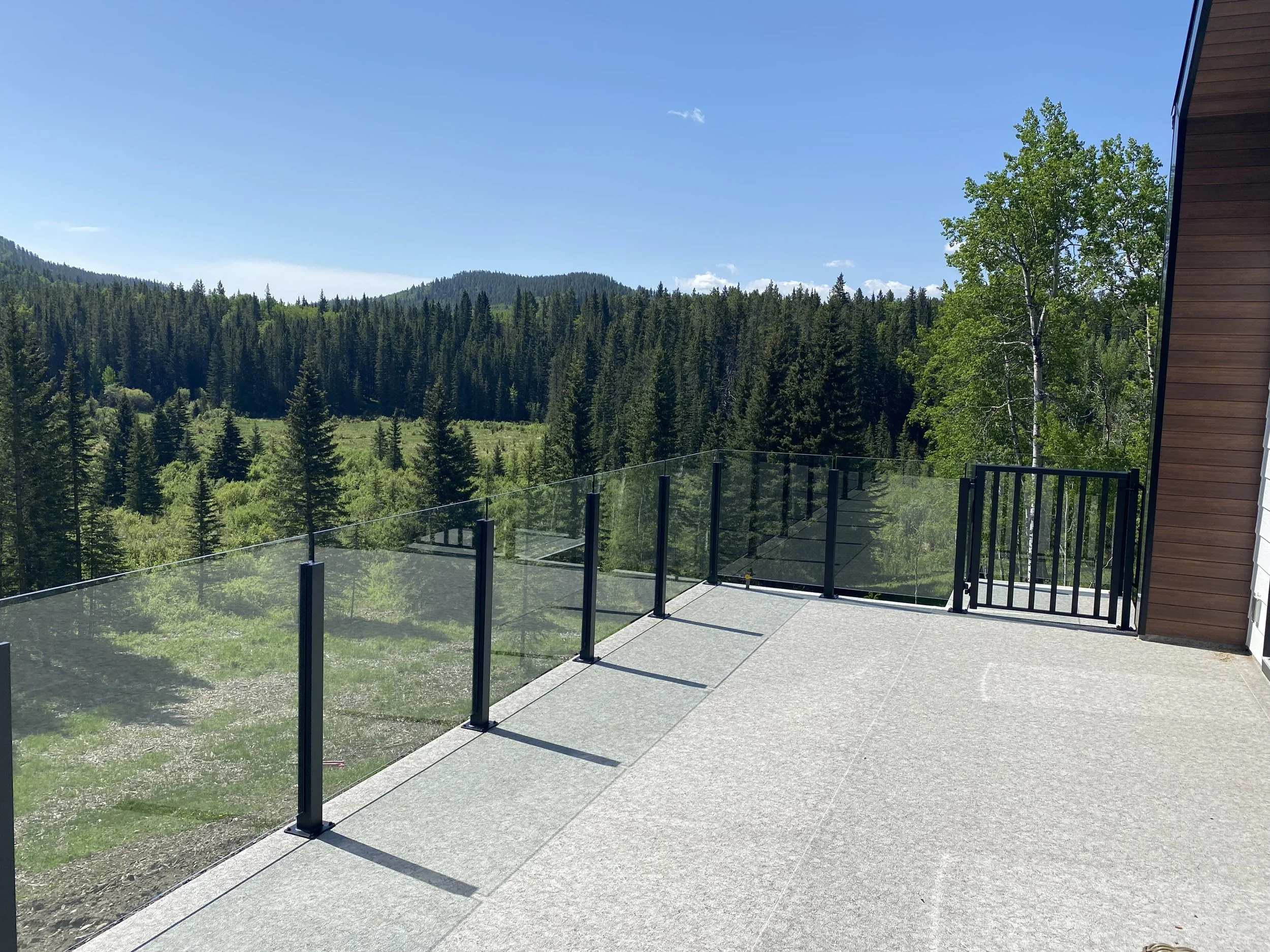 A view of a residential balcony overlooking a forested mountain landscape on a clear, sunny day.