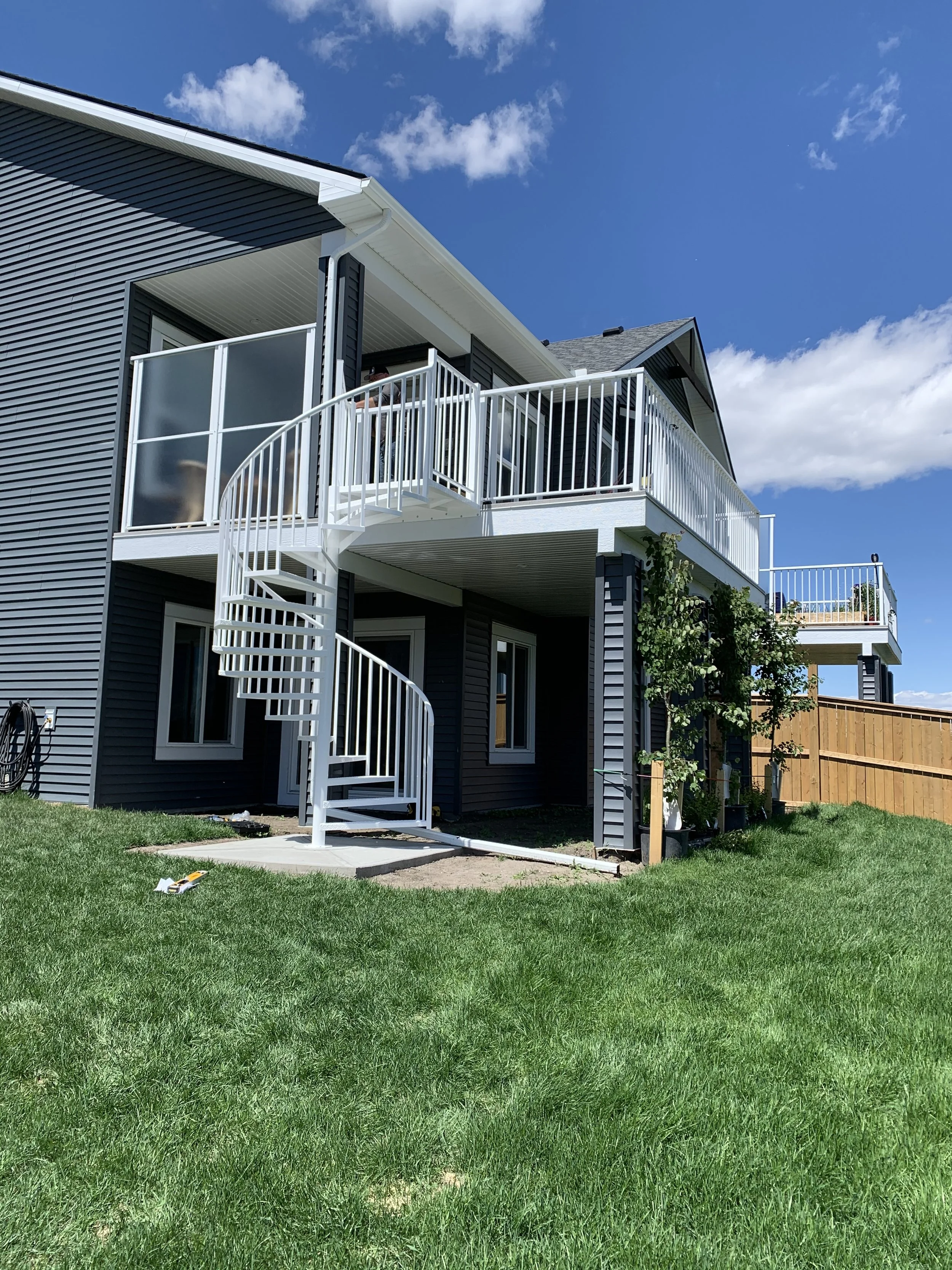Residential building with white metal spiral staircase leading to a second-floor balcony under a blue sky with clouds.