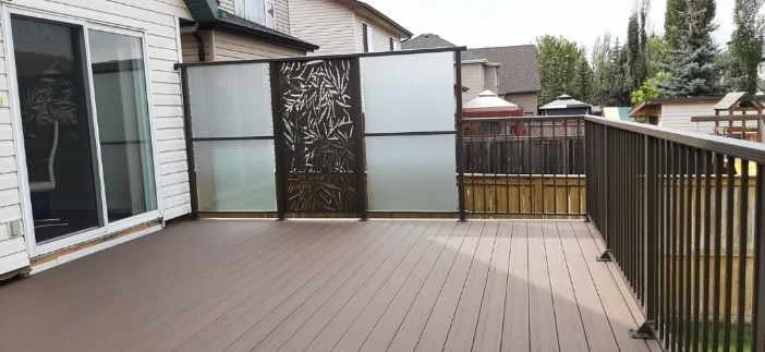 Empty outdoor deck with wooden flooring and a decorative privacy screen at the far end, enclosed by a black metal railing.