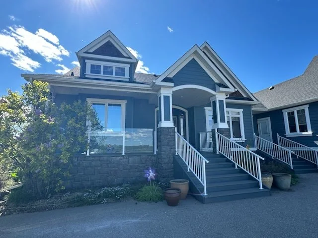 Front view of a modern blue house with a porch, white railings, and stairs, under a sunny sky.