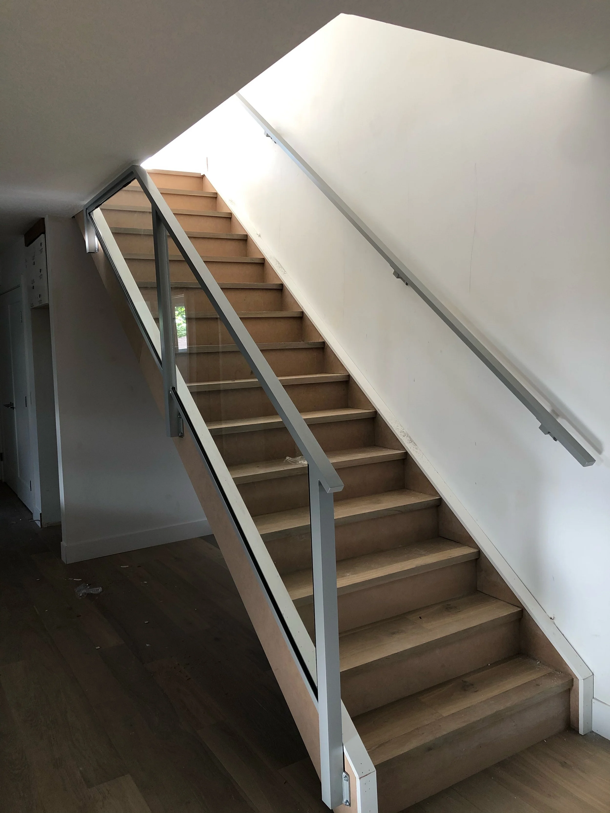 An indoor wooden staircase with metal handrails ascending to an upper floor, illuminated by natural light from a skylight.
