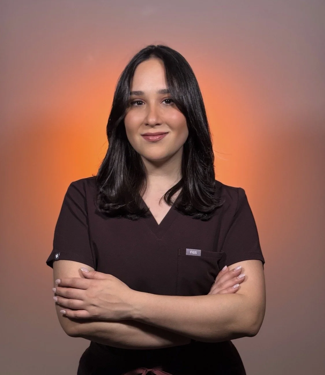 A woman with dark hair and a black uniform standing with arms crossed against a warm, gradient background.