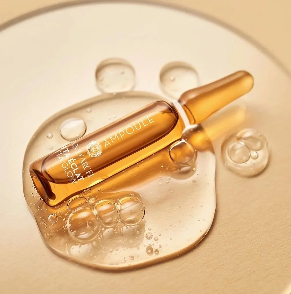 A golden ampoule lies on a reflective surface, surrounded by liquid and air bubbles.