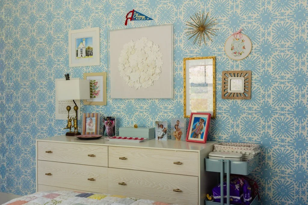 Decorative bedroom wall with picture frames, mirror, wall art, and a dresser with framed photos and a small teal organizer.