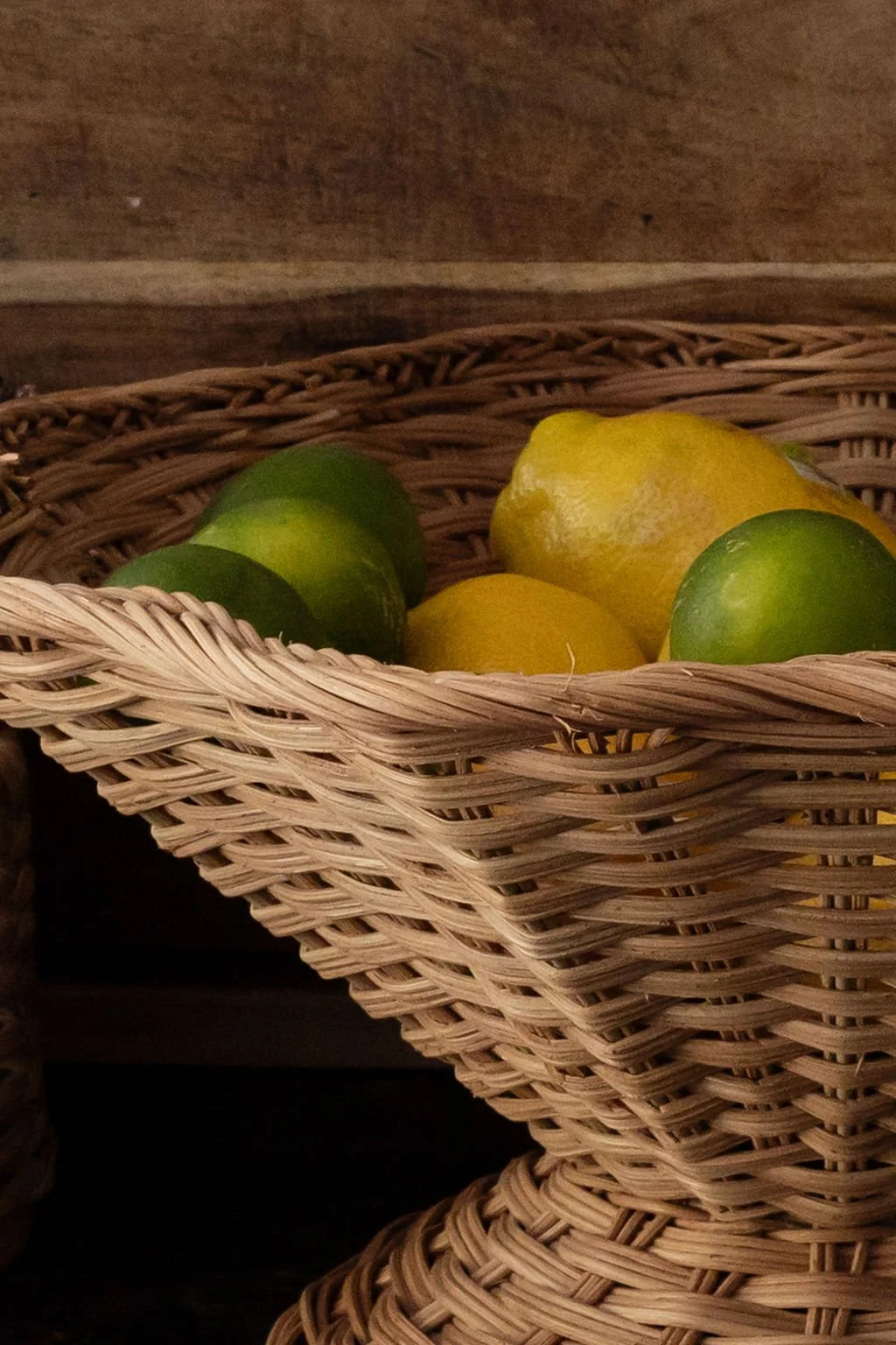 Basket filled with yellow and green lemons, set on a wooden surface.