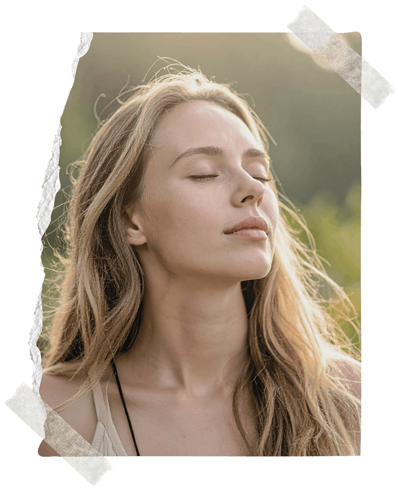 A blonde woman taking a beep breath of fresh air with her eyes closed outside