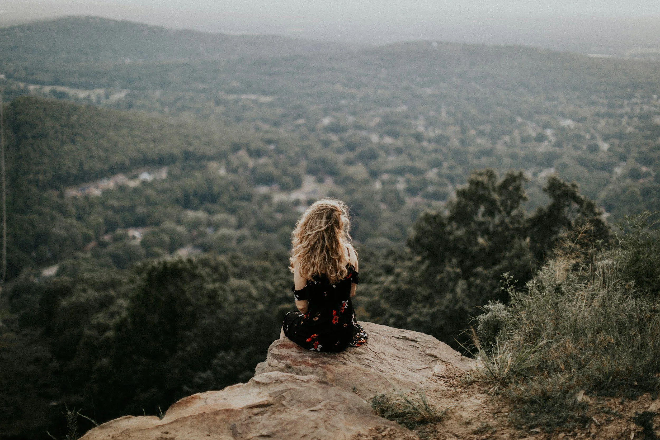 A woman sitting on the edge of a cliff looking out onto the landscape