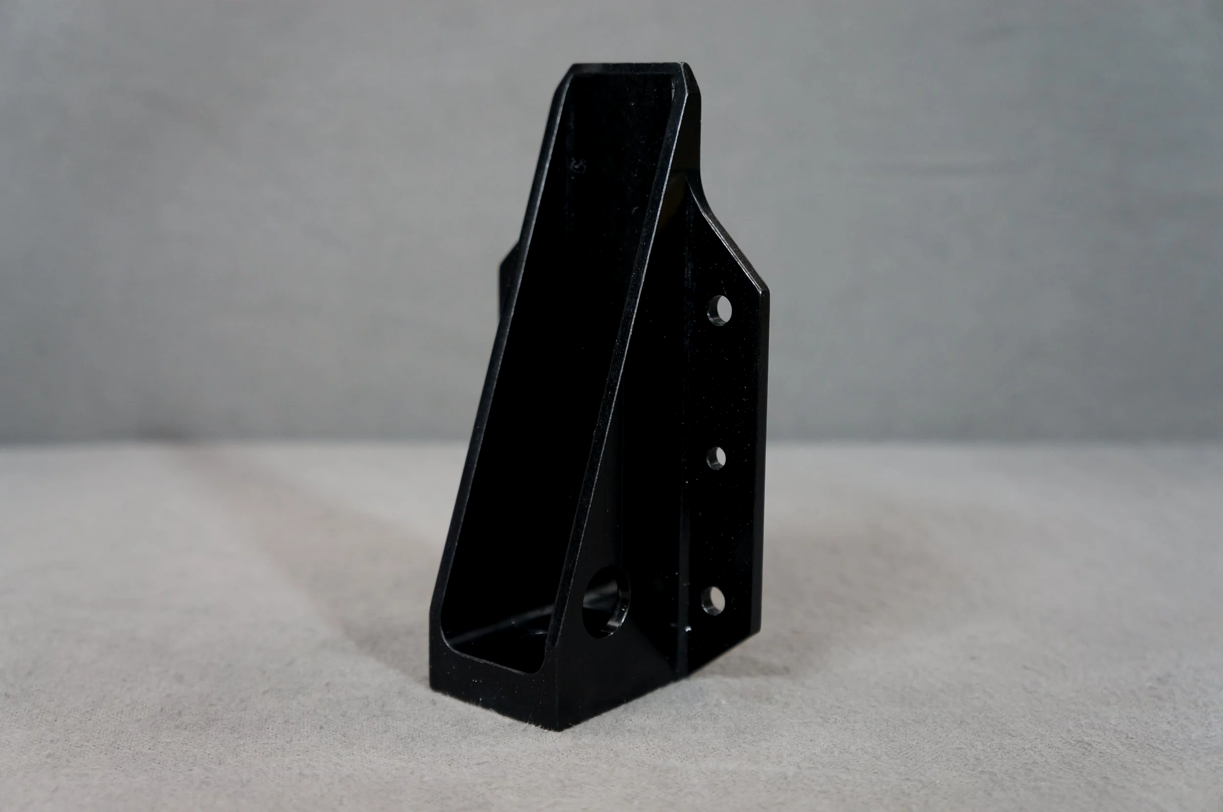 Black metal L-shaped bracket with multiple holes, standing upright on a light surface against a plain background.