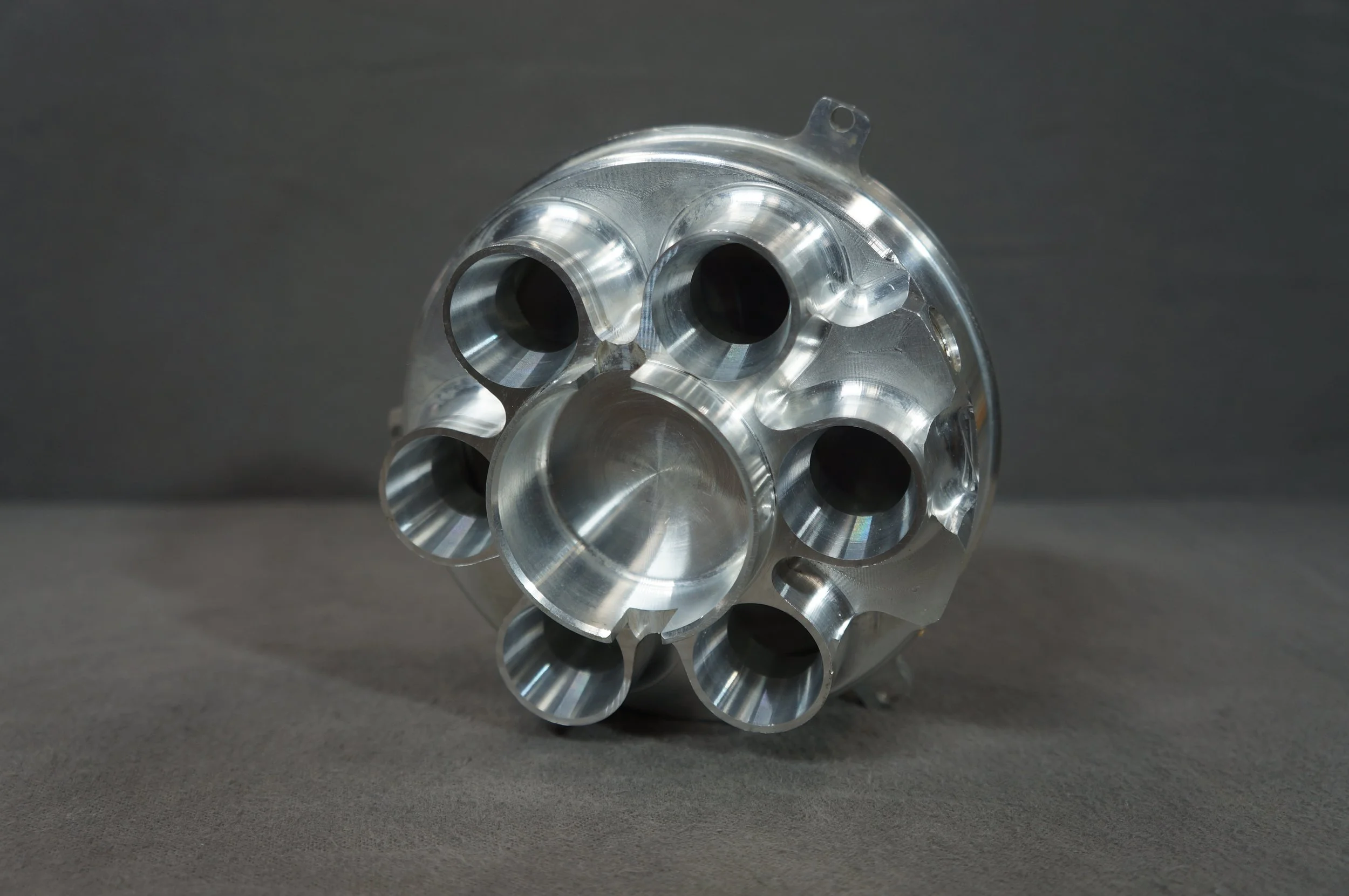 A metallic, machined turbine or engine part with multiple hollow cylindrical openings, reflecting light, placed on a dark surface.