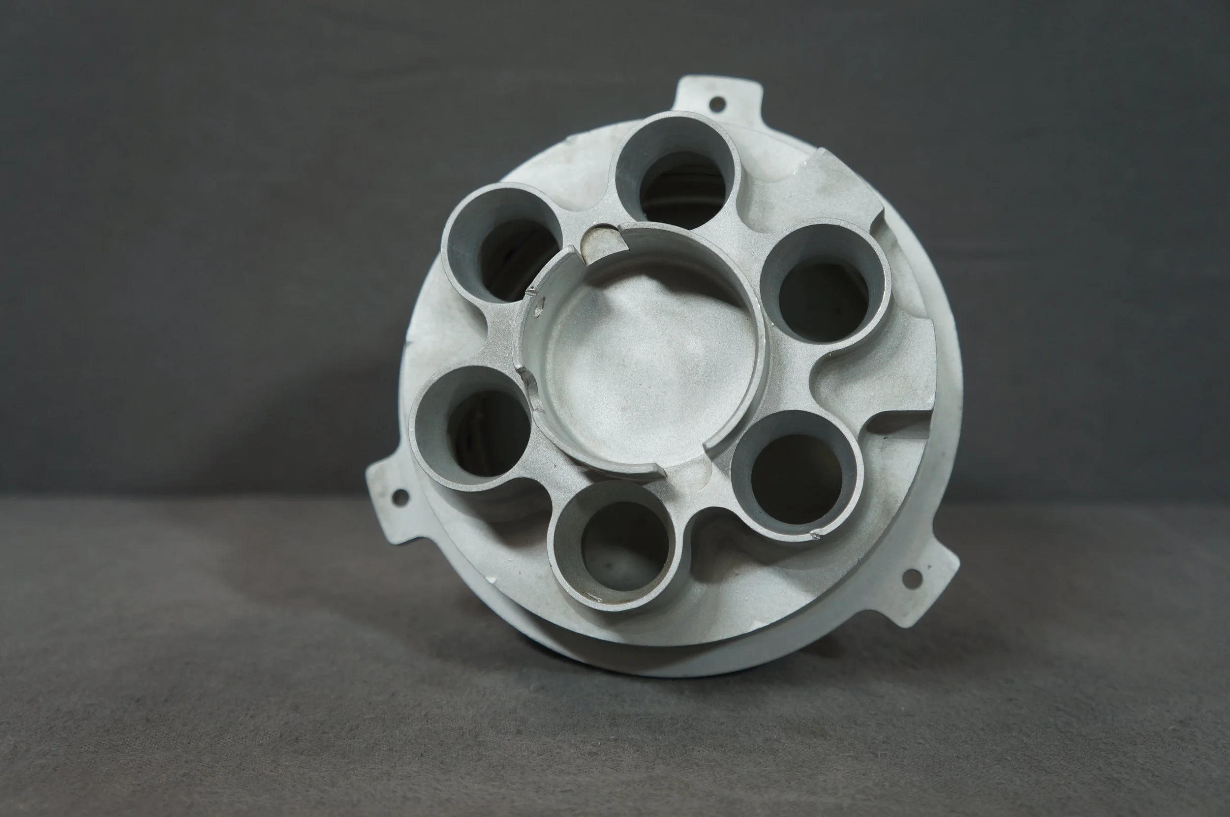 Metal engine part with multiple cylindrical openings placed on a dark surface.
