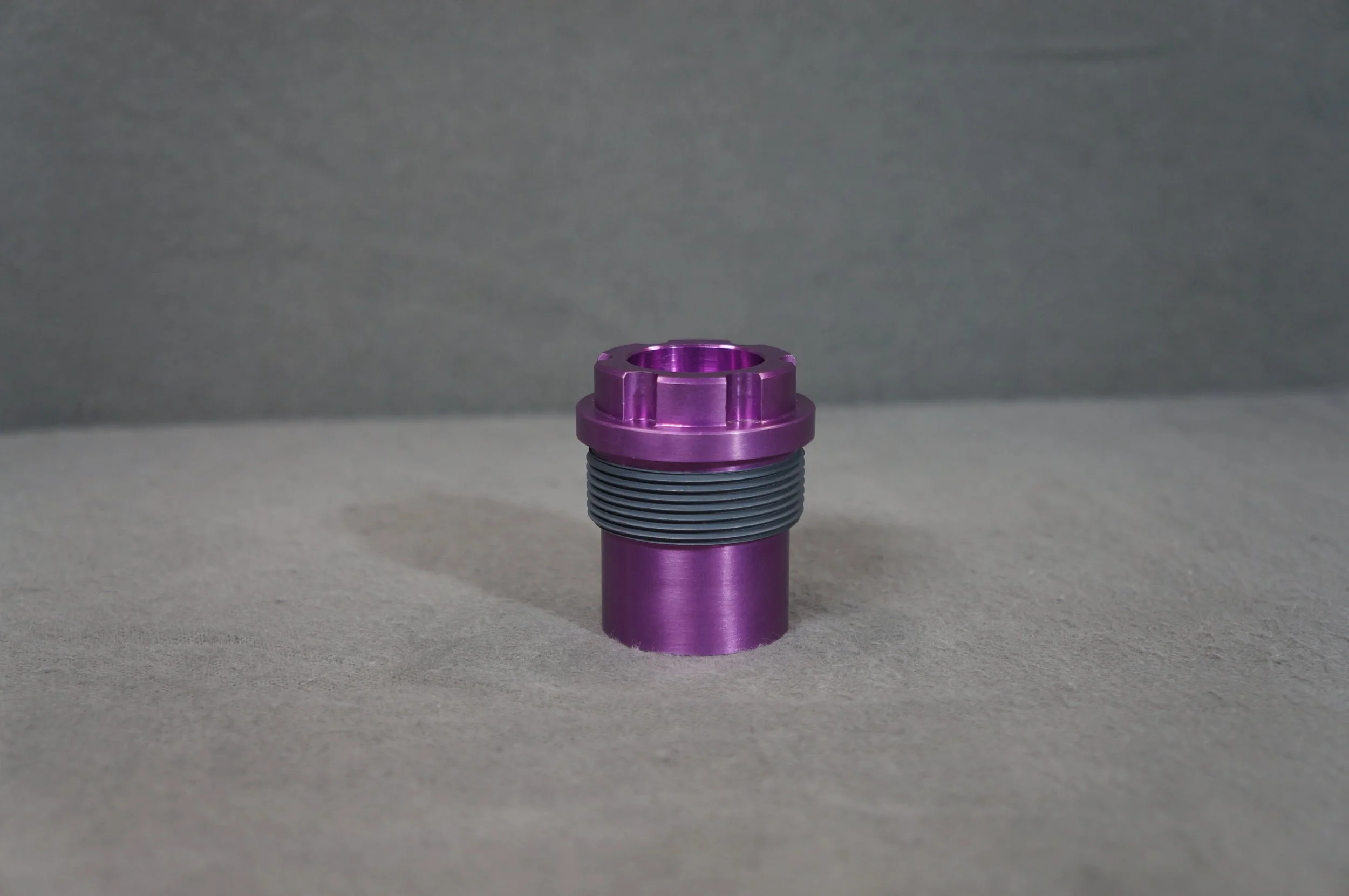 A metallic purple cylindrical object with a threaded section near the top, placed on a gray surface with a gray background.