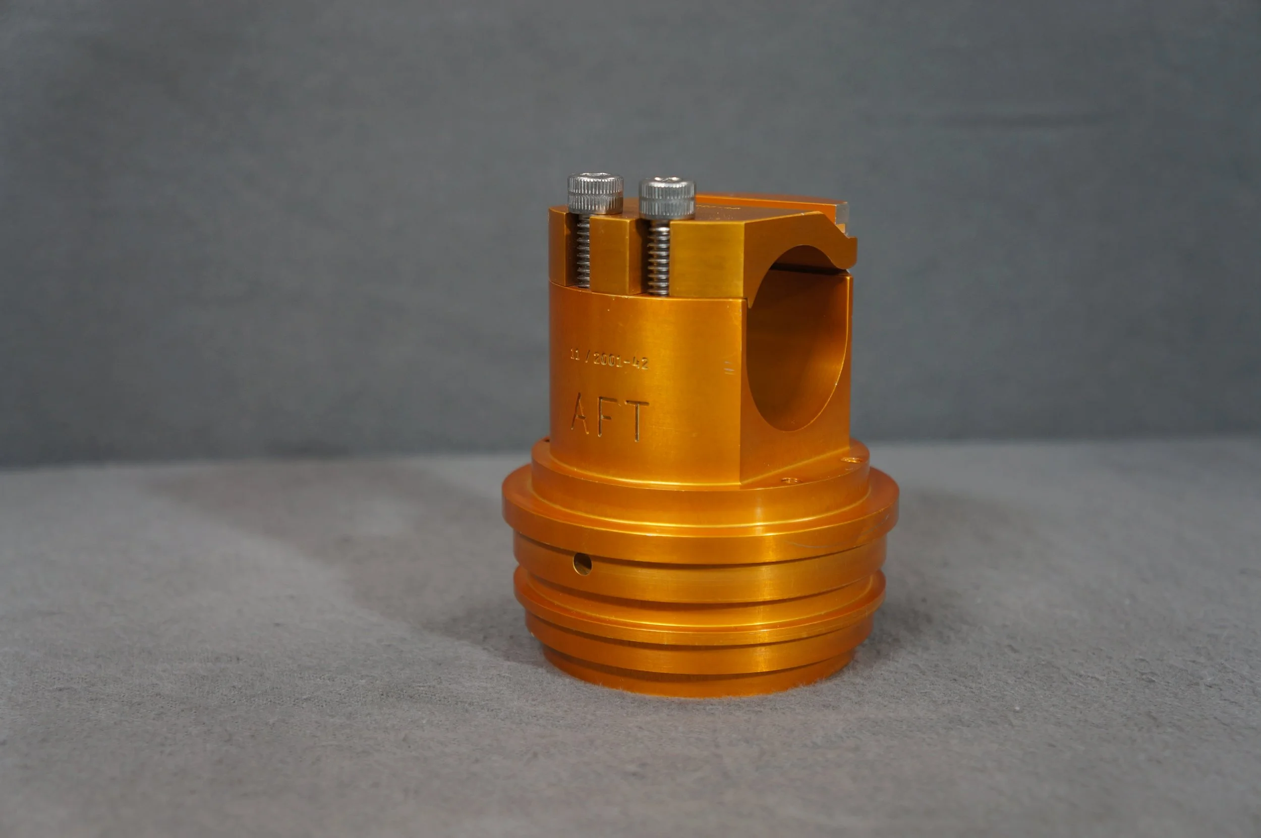 A close-up of an orange metal mechanical component with two silver screws on top and engraved markings, set against a gray background.